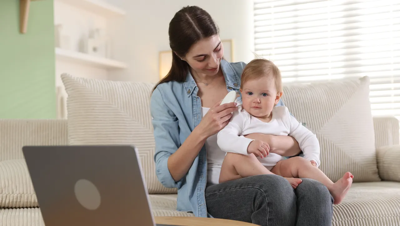 A mother holding her baby on the sofa during a video call on a laptop